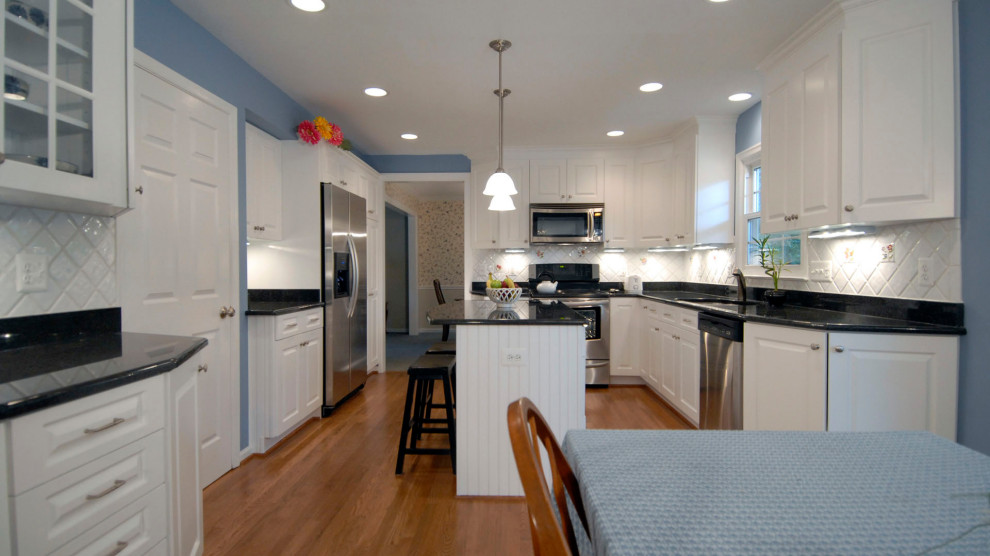 ボストンにある中くらいなカントリー風のおしゃれなキッチン (ドロップインシンク、レイズドパネル扉のキャビネット、白いキャビネット、オニキスカウンター、白いキッチンパネル、セラミックタイルのキッチンパネル、シルバーの調理設備、淡色無垢フローリング、茶色い床、黒いキッチンカウンター) の写真