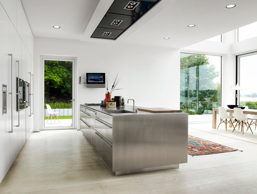 Design ideas for a large contemporary open plan kitchen in London with an integrated sink, flat-panel cabinets, stainless steel cabinets, stainless steel benchtops, stainless steel appliances, light hardwood floors and with island.