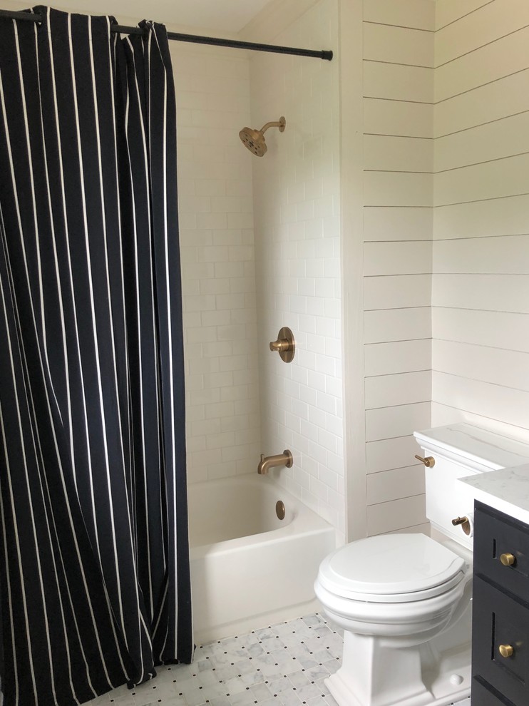 Photo of a small contemporary bathroom in Nashville with raised-panel cabinets, black cabinets, an alcove tub, a shower/bathtub combo, a one-piece toilet, white tile, ceramic tile, white walls, marble floors, an undermount sink, engineered quartz benchtops, white floor, a shower curtain and white benchtops.