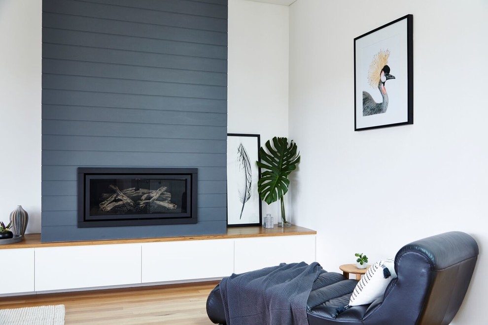Photo of a contemporary open concept living room in Sydney with white walls, light hardwood floors, a standard fireplace, a wood fireplace surround and no tv.