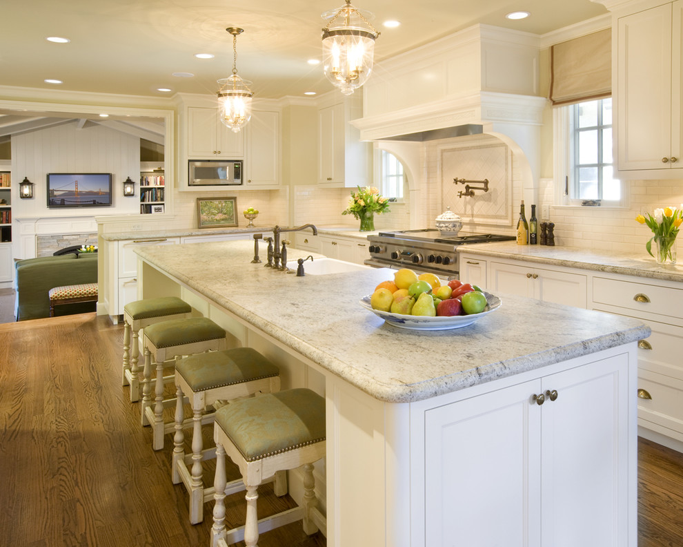 Inspiration for a traditional l-shaped eat-in kitchen in San Francisco with a farmhouse sink, recessed-panel cabinets, white cabinets, granite benchtops, white splashback, subway tile splashback and stainless steel appliances.