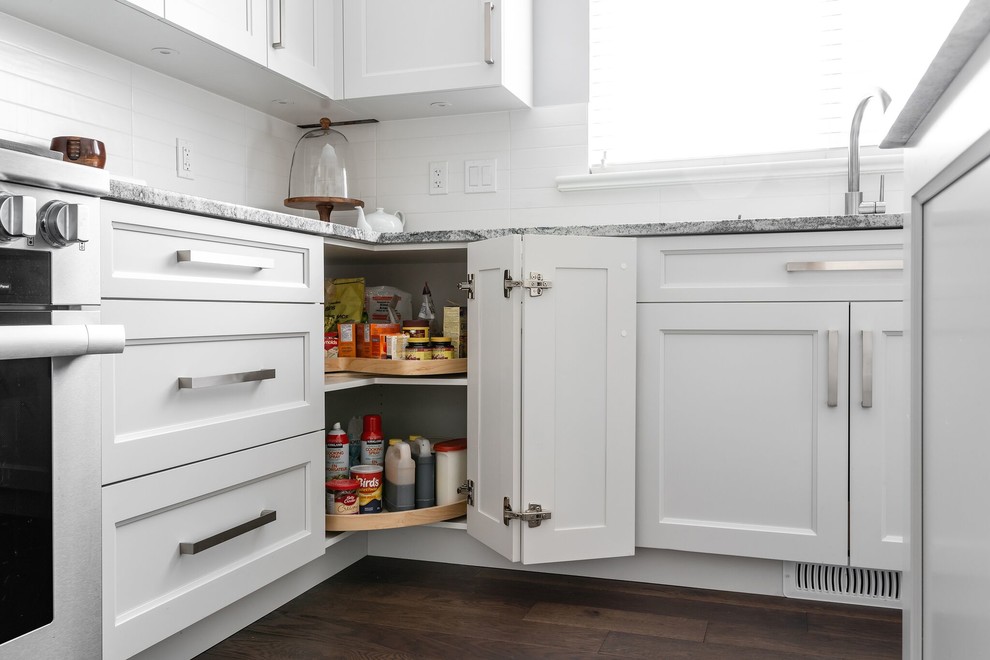 Large transitional u-shaped medium tone wood floor and brown floor eat-in kitchen photo in Vancouver with an undermount sink, recessed-panel cabinets, white cabinets, granite countertops, white backsplash, subway tile backsplash, stainless steel appliances, an island and multicolored countertops