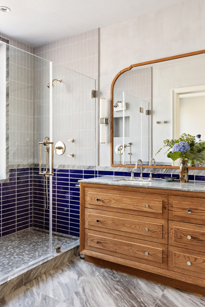 Inspiration for a transitional blue tile and cement tile marble floor, gray floor and double-sink double shower remodel in New York with furniture-like cabinets, medium tone wood cabinets, gray walls, an undermount sink, marble countertops, a hinged shower door, gray countertops and a built-in vanity
