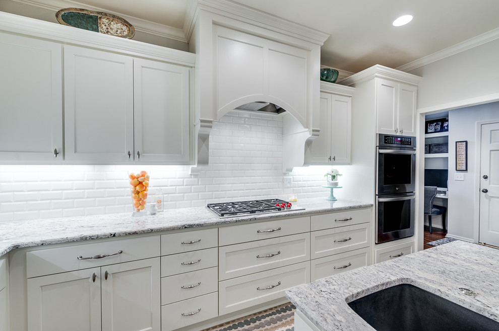 Inspiration for a large transitional u-shaped eat-in kitchen in Kansas City with an undermount sink, glass-front cabinets, white cabinets, granite benchtops, white splashback, subway tile splashback, stainless steel appliances, dark hardwood floors and with island.