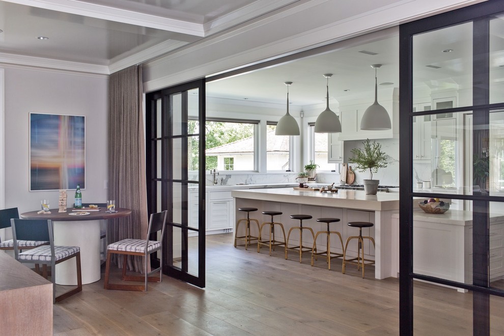Example of a large transitional medium tone wood floor and brown floor eat-in kitchen design with an undermount sink, recessed-panel cabinets, white cabinets, marble countertops, white backsplash, marble backsplash, stainless steel appliances, an island and white countertops
