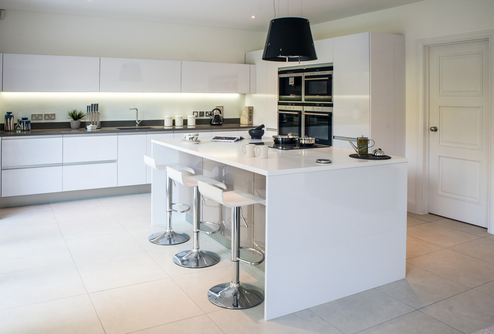 Inspiration for a large contemporary l-shaped open plan kitchen in Other with a drop-in sink, flat-panel cabinets, white cabinets, quartzite benchtops, white splashback, glass tile splashback, stainless steel appliances, porcelain floors and with island.