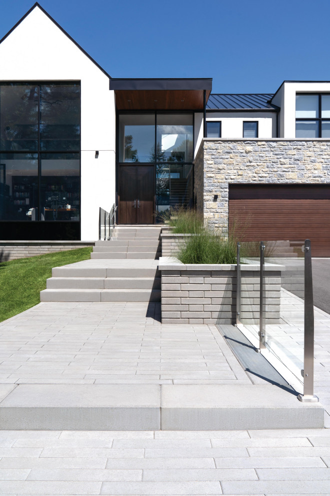 This is an example of a mid-sized modern front yard full sun driveway with a retaining wall, concrete pavers and a metal fence.