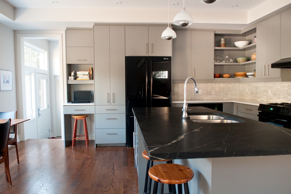 This is an example of a modern eat-in kitchen in Toronto with a double-bowl sink, black appliances, soapstone benchtops, flat-panel cabinets, grey cabinets, white splashback and stone tile splashback.