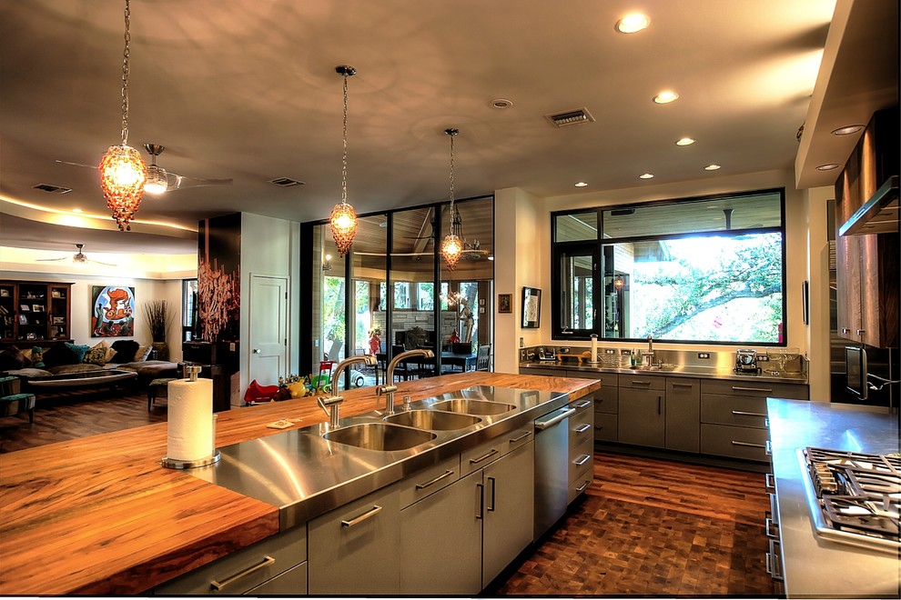 Design ideas for a large eclectic galley open plan kitchen in Austin with a triple-bowl sink, flat-panel cabinets, grey cabinets, wood benchtops, beige splashback and stainless steel appliances.