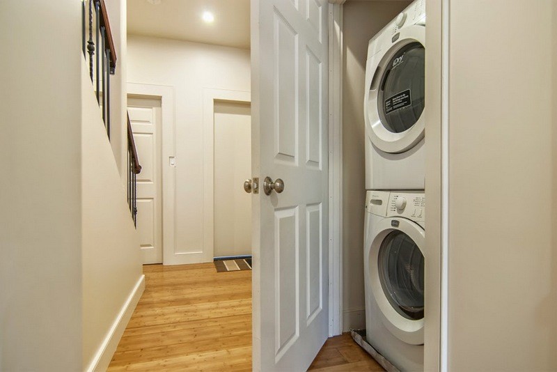 Small single-wall laundry cupboard in San Francisco with a stacked washer and dryer, beige walls and bamboo floors.