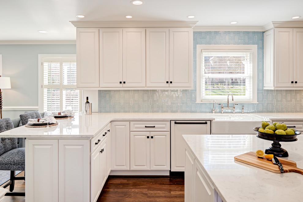 Mid-sized transitional u-shaped medium tone wood floor and brown floor eat-in kitchen photo with a farmhouse sink, raised-panel cabinets, white cabinets, quartz countertops, blue backsplash, porcelain backsplash, paneled appliances and an island