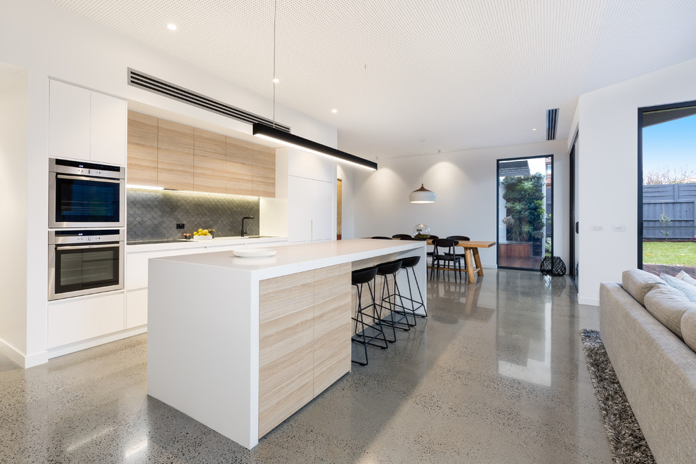 Contemporary galley eat-in kitchen in Melbourne with an undermount sink, flat-panel cabinets, white cabinets, solid surface benchtops, grey splashback, stone tile splashback, stainless steel appliances, concrete floors and with island.