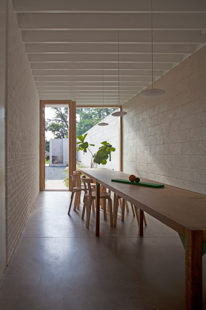 Exemple d'une salle à manger ouverte sur la cuisine rétro de taille moyenne avec un mur blanc, sol en béton ciré, un manteau de cheminée en béton, un sol beige, poutres apparentes et un mur en parement de brique.