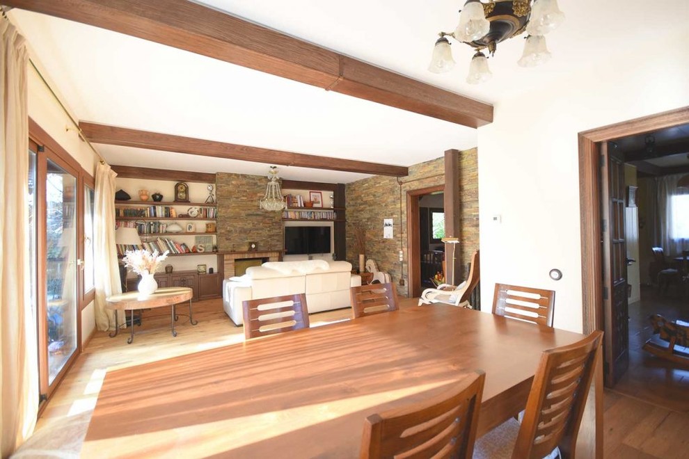 Ejemplo de comedor rústico de tamaño medio abierto con paredes blancas, suelo de madera en tonos medios, todas las chimeneas, marco de chimenea de ladrillo y suelo marrón