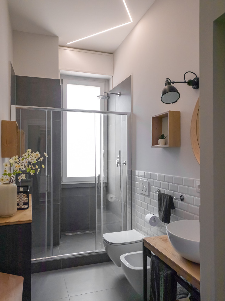 Medium sized industrial shower room bathroom in Milan with open cabinets, light wood cabinets, an alcove shower, a two-piece toilet, white tiles, porcelain tiles, grey walls, porcelain flooring, a vessel sink, wooden worktops, grey floors, a sliding door, a single sink, a freestanding vanity unit and a drop ceiling.