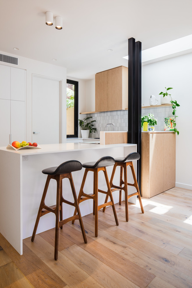 Design ideas for a contemporary u-shaped kitchen in Melbourne with flat-panel cabinets, medium wood cabinets, white splashback, medium hardwood floors, a peninsula, brown floor and white benchtop.