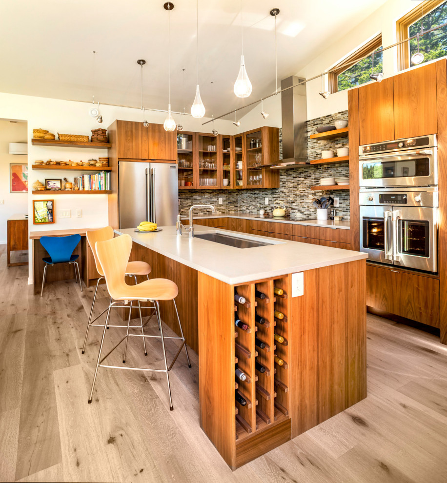 Photo of a large midcentury l-shaped open plan kitchen in Seattle with an undermount sink, flat-panel cabinets, medium wood cabinets, quartz benchtops, multi-coloured splashback, glass tile splashback, stainless steel appliances, with island, white benchtop, light hardwood floors and grey floor.