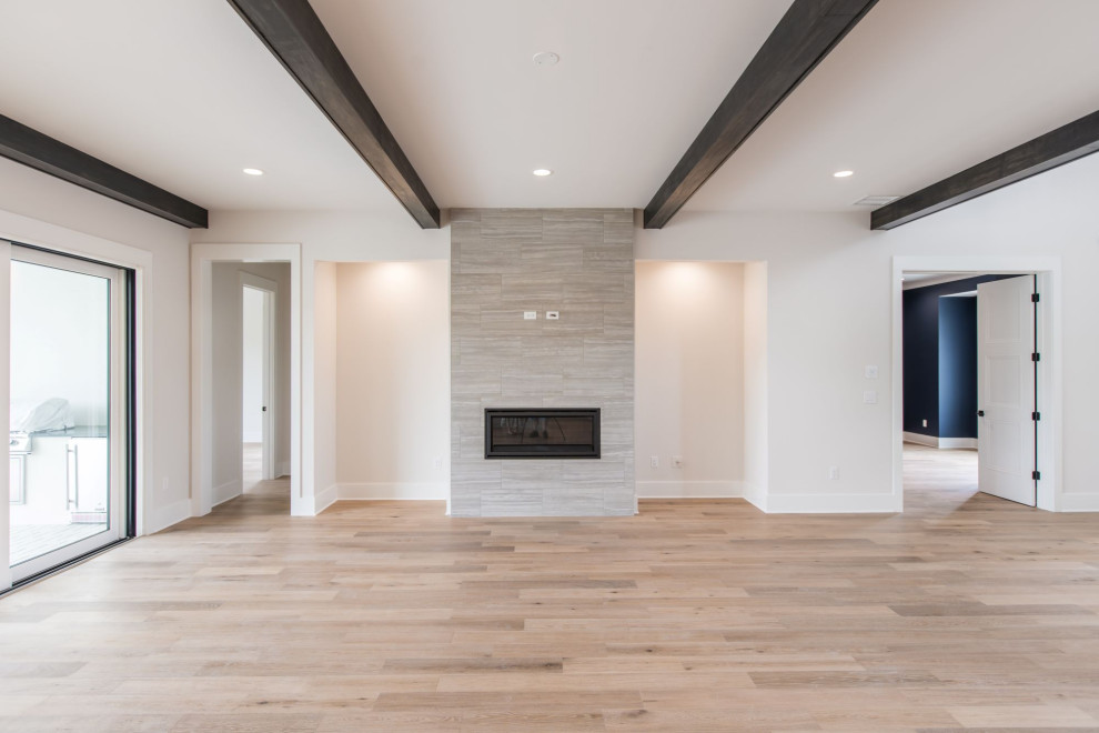 Inspiration for a large classic open plan games room in Jacksonville with white walls, light hardwood flooring, a standard fireplace, a tiled fireplace surround, a wall mounted tv, brown floors and exposed beams.