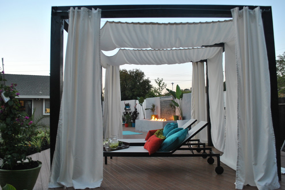 This is an example of a mid-sized tropical backyard deck in Sacramento with a fire feature and a pergola.