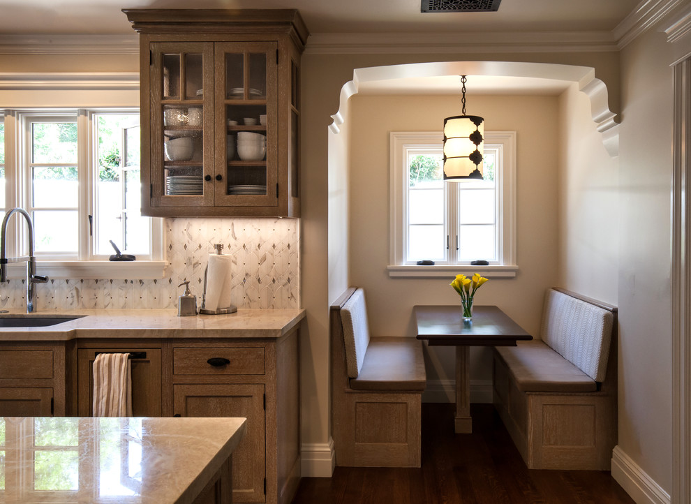 This is an example of a mid-sized mediterranean u-shaped eat-in kitchen in Santa Barbara with an integrated sink, beige cabinets, quartzite benchtops, white splashback, mosaic tile splashback, stainless steel appliances, medium hardwood floors, with island and glass-front cabinets.