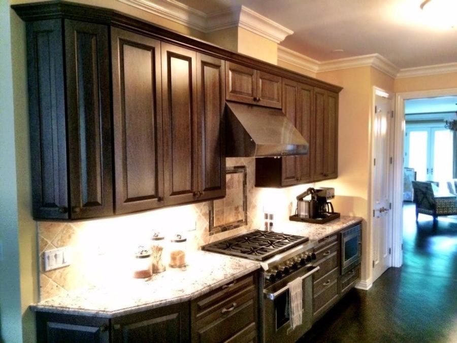 Mid-sized transitional galley medium tone wood floor enclosed kitchen photo in Chicago with a double-bowl sink, raised-panel cabinets, dark wood cabinets, quartz countertops, white backsplash, stone tile backsplash, stainless steel appliances and an island
