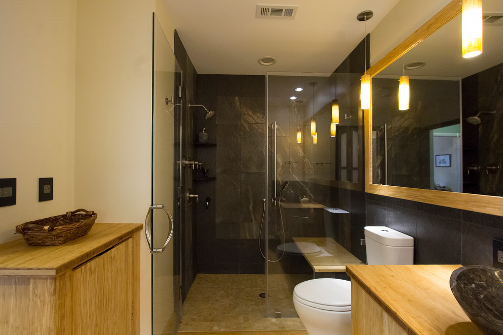 Inspiration for a mid-sized contemporary master bathroom in Raleigh with a vessel sink, light wood cabinets, wood benchtops, a curbless shower, a two-piece toilet, porcelain tile, yellow walls, flat-panel cabinets, black tile, bamboo floors, yellow floor, a hinged shower door and yellow benchtops.