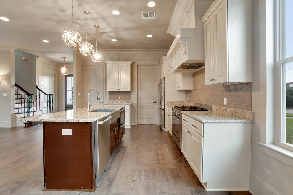 Design ideas for a mid-sized traditional l-shaped open plan kitchen in New Orleans with a farmhouse sink, raised-panel cabinets, white cabinets, beige splashback, stainless steel appliances, medium hardwood floors and with island.