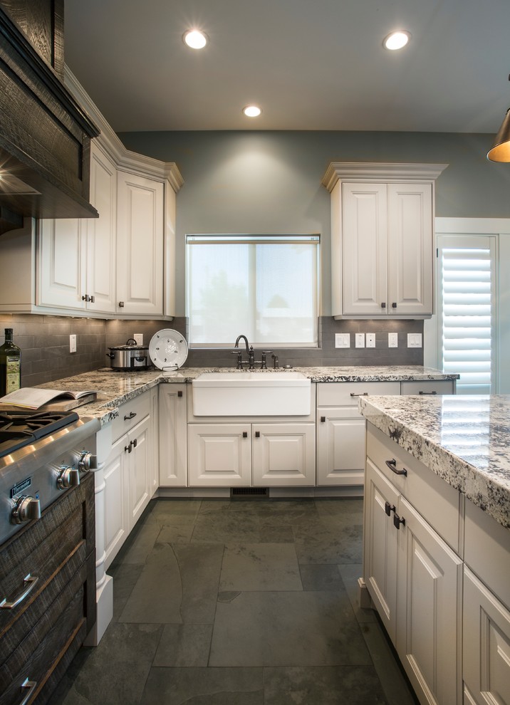 This is an example of a mid-sized country u-shaped eat-in kitchen in Salt Lake City with a farmhouse sink, raised-panel cabinets, white cabinets, granite benchtops, grey splashback, subway tile splashback, stainless steel appliances, slate floors, with island and multi-coloured benchtop.