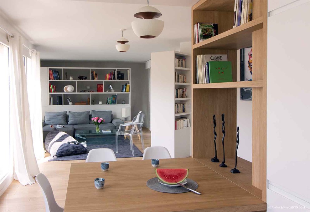 Cette image montre une salle de séjour design de taille moyenne et ouverte avec une bibliothèque ou un coin lecture, un mur blanc, parquet clair, un téléviseur dissimulé, aucune cheminée et un sol marron.