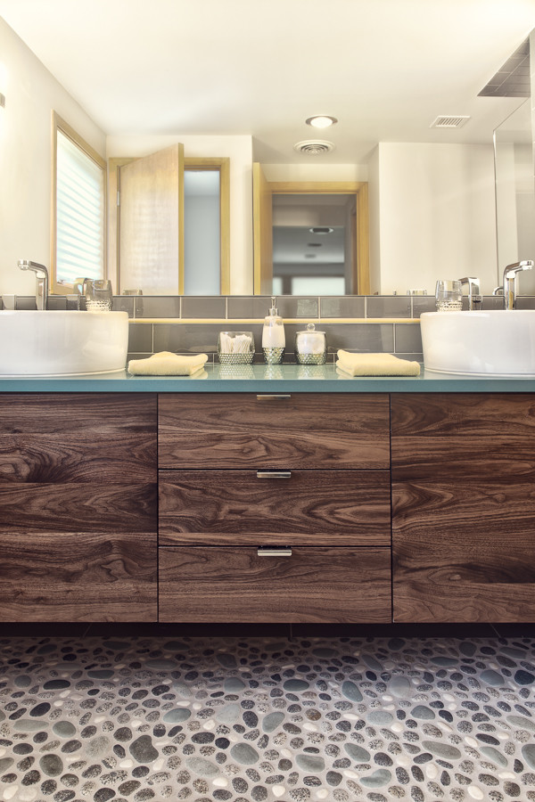 This is an example of a mid-sized midcentury master bathroom in Detroit with a vessel sink, flat-panel cabinets, medium wood cabinets, engineered quartz benchtops, gray tile, subway tile and pebble tile floors.