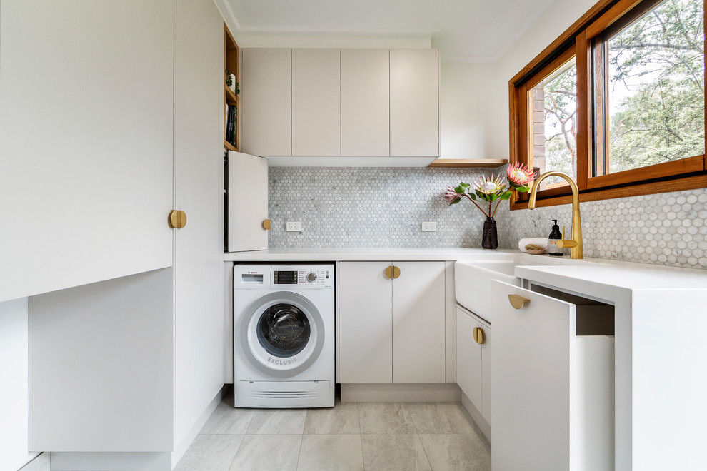 Photo of a mid-sized contemporary u-shaped utility room in Melbourne with a farmhouse sink, flat-panel cabinets, white cabinets, quartz benchtops, white walls, porcelain floors, a side-by-side washer and dryer, grey floor and white benchtop.