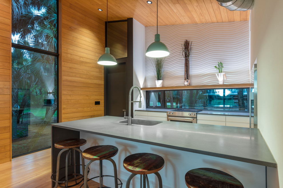 Small contemporary single-wall open plan kitchen in Other with an integrated sink, flat-panel cabinets, white cabinets, concrete benchtops, window splashback, stainless steel appliances, light hardwood floors, a peninsula, multi-coloured floor, grey benchtop and wood.