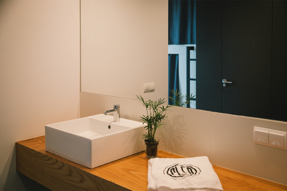 Modelo de cuarto de baño principal y único moderno grande con armarios abiertos, puertas de armario blancas, ducha a ras de suelo, sanitario de una pieza, baldosas y/o azulejos blancos, baldosas y/o azulejos de cerámica, paredes blancas, suelo de baldosas de cerámica, lavabo sobreencimera, encimera de madera, suelo negro, ducha con puerta con bisagras y cuarto de baño