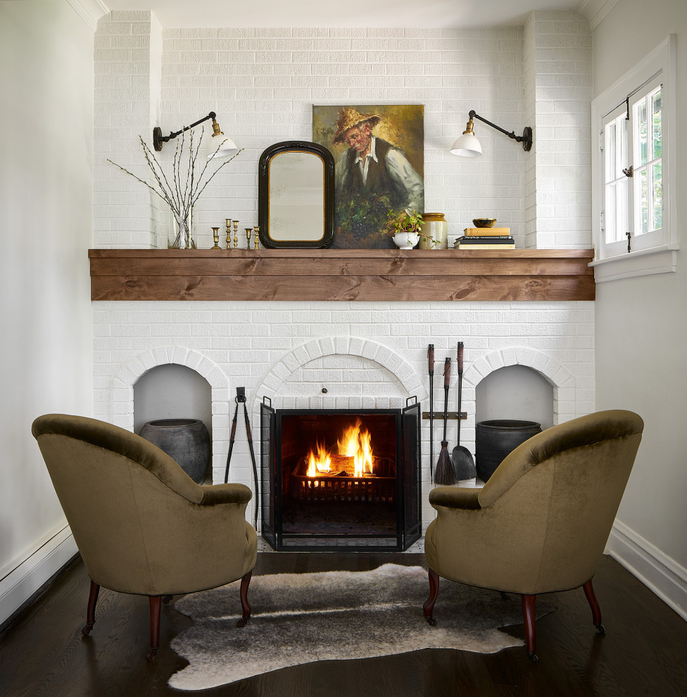 Photo of a small transitional living room in Chicago with white walls, dark hardwood floors, a standard fireplace, a brick fireplace surround, no tv, brown floor and brick walls.