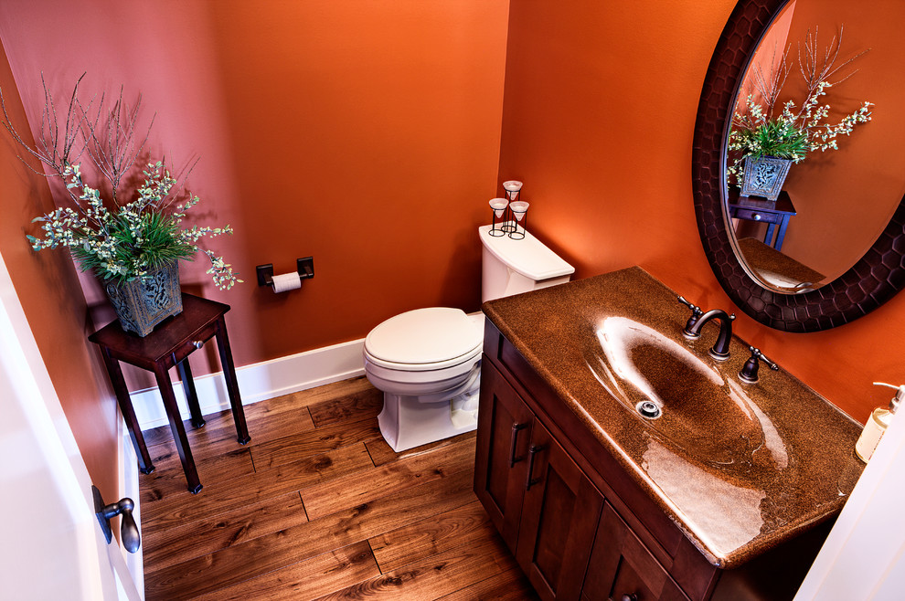 Inspiration for a mid-sized arts and crafts powder room in Calgary with shaker cabinets, medium wood cabinets, a two-piece toilet, orange walls, medium hardwood floors, an integrated sink and engineered quartz benchtops.