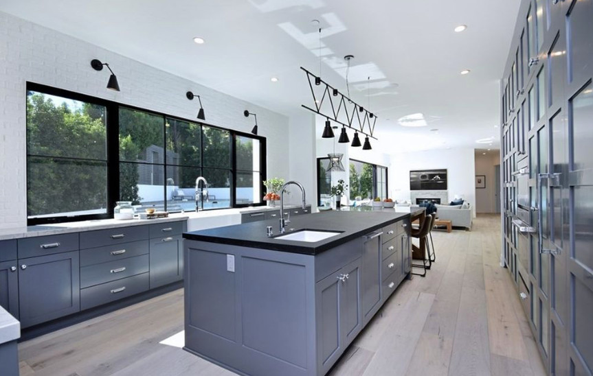 Design ideas for an expansive country u-shaped eat-in kitchen in Los Angeles with a farmhouse sink, shaker cabinets, grey cabinets, granite benchtops, white splashback, brick splashback, stainless steel appliances, medium hardwood floors, with island, grey floor and white benchtop.