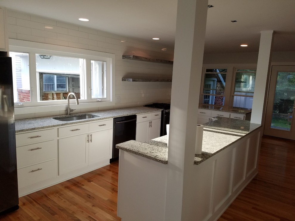 Open concept kitchen - mid-sized transitional l-shaped medium tone wood floor and brown floor open concept kitchen idea with an undermount sink, recessed-panel cabinets, white cabinets, granite countertops, white backsplash, subway tile backsplash, black appliances, an island and beige countertops