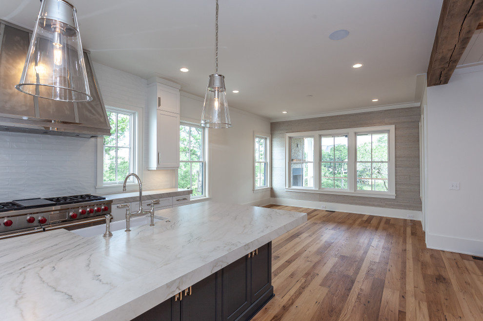 Photo of an expansive beach style l-shaped open plan kitchen in Charleston with a farmhouse sink, beaded inset cabinets, blue cabinets, quartzite benchtops, white splashback, subway tile splashback, stainless steel appliances, light hardwood floors, with island and white benchtop.