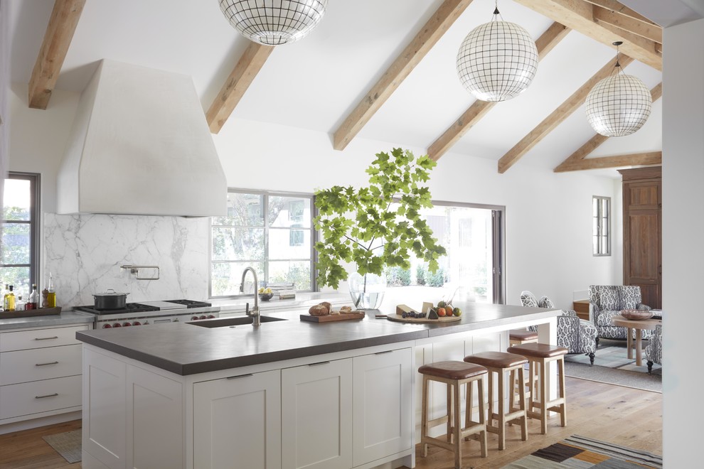 Inspiration for a beach style open plan kitchen in San Francisco with a single-bowl sink, white cabinets, white splashback, stone slab splashback, stainless steel appliances, light hardwood floors, with island and grey benchtop.