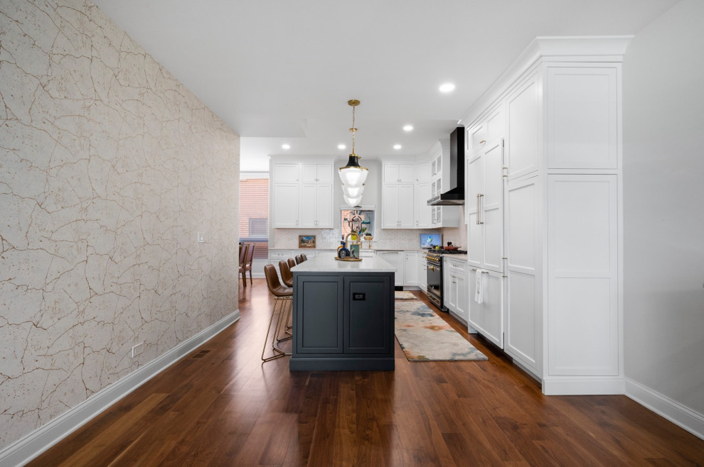 This is an example of a large contemporary l-shaped kitchen pantry in Chicago with a belfast sink, shaker cabinets, white cabinets, quartz worktops, beige splashback, mosaic tiled splashback, black appliances, dark hardwood flooring, an island and beige worktops.