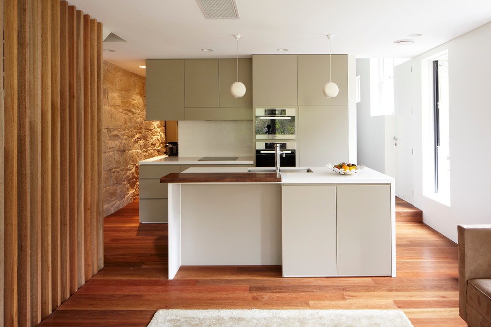 Inspiration for a mid-sized contemporary galley open plan kitchen in Sydney with an undermount sink, flat-panel cabinets, green cabinets, solid surface benchtops, white splashback, glass sheet splashback, stainless steel appliances, medium hardwood floors and with island.