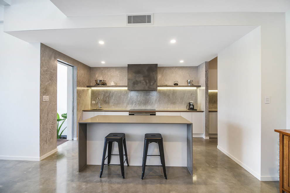 Photo of a contemporary single-wall kitchen in Sunshine Coast with an undermount sink, flat-panel cabinets, white cabinets, grey splashback, black appliances, concrete floors, with island, grey floor and grey benchtop.