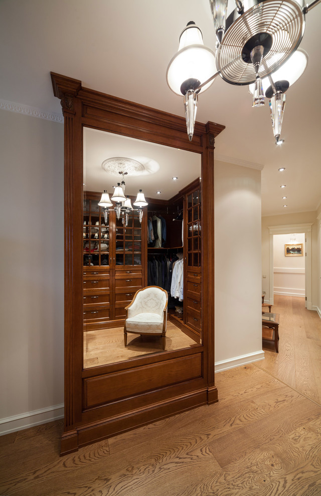 Photo of a mid-sized traditional gender-neutral walk-in wardrobe in Moscow with recessed-panel cabinets, dark wood cabinets, medium hardwood floors and brown floor.