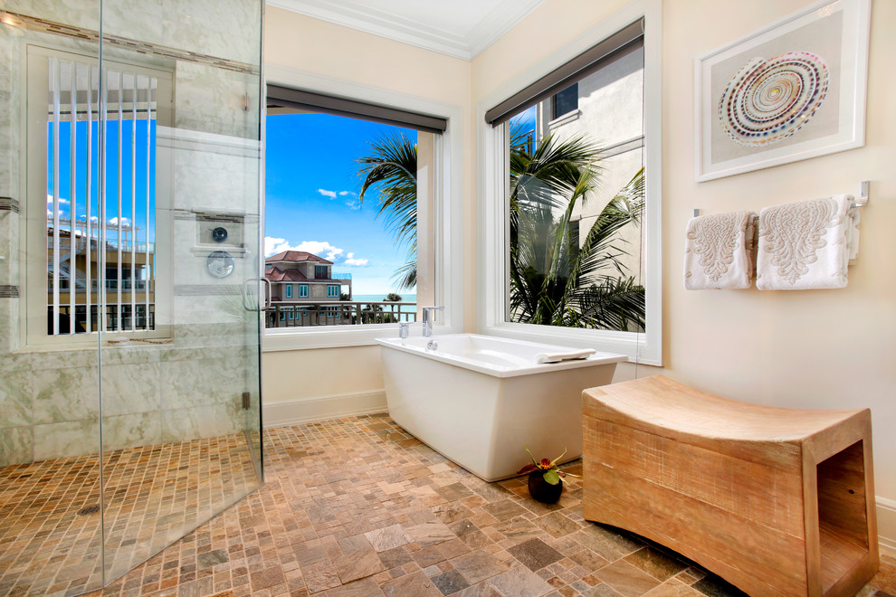 Inspiration for a tropical master bathroom in Miami with a freestanding tub, a curbless shower, brown tile, beige walls and a hinged shower door.