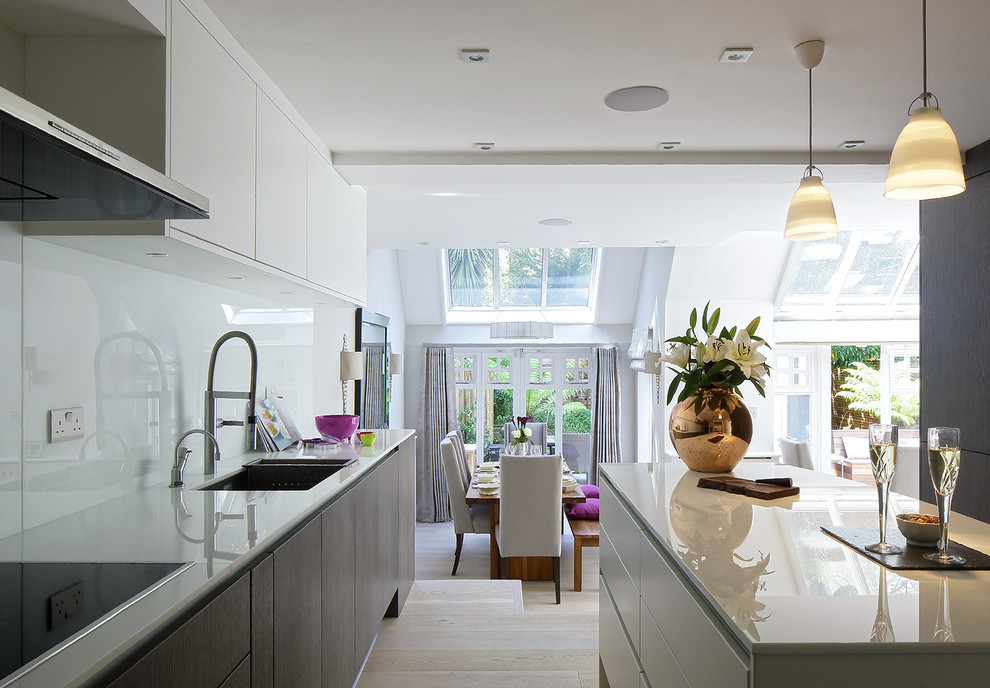 Contemporary open plan kitchen in London with an undermount sink, flat-panel cabinets, white splashback and with island.