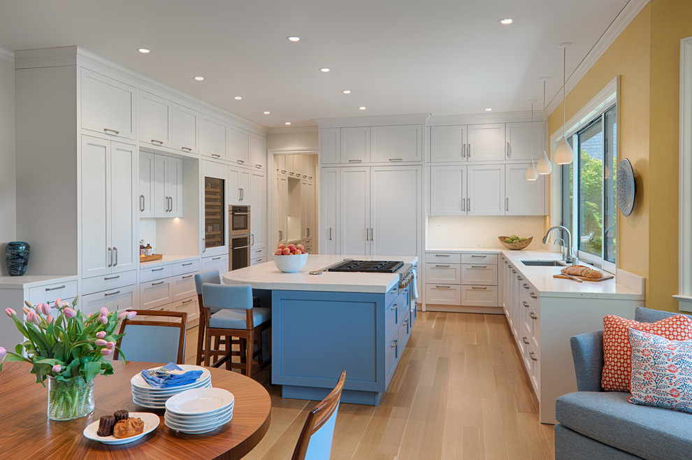 This is an example of a large transitional u-shaped eat-in kitchen in San Francisco with an undermount sink, shaker cabinets, white cabinets, white splashback, stone slab splashback, light hardwood floors, with island, beige floor, white benchtop, solid surface benchtops and panelled appliances.