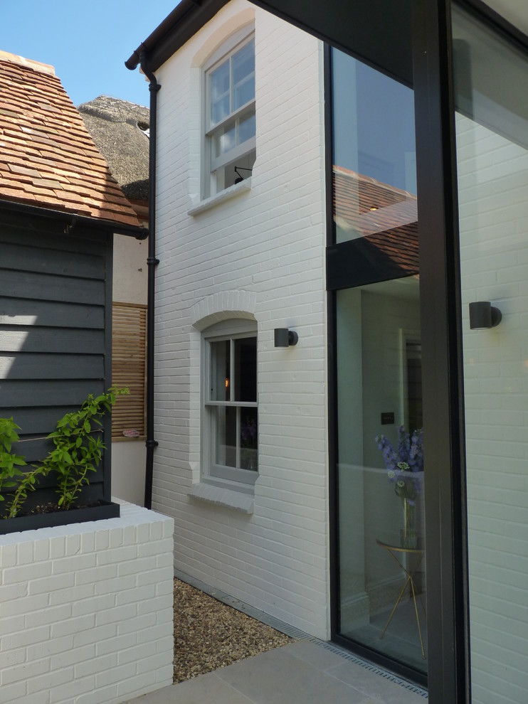 This is an example of a large transitional two-storey brick white house exterior in Berkshire with a gable roof and a tile roof.