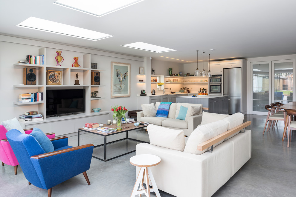 This is an example of a mid-sized transitional open concept family room in Hampshire with white walls, concrete floors, no fireplace, a built-in media wall and a library.