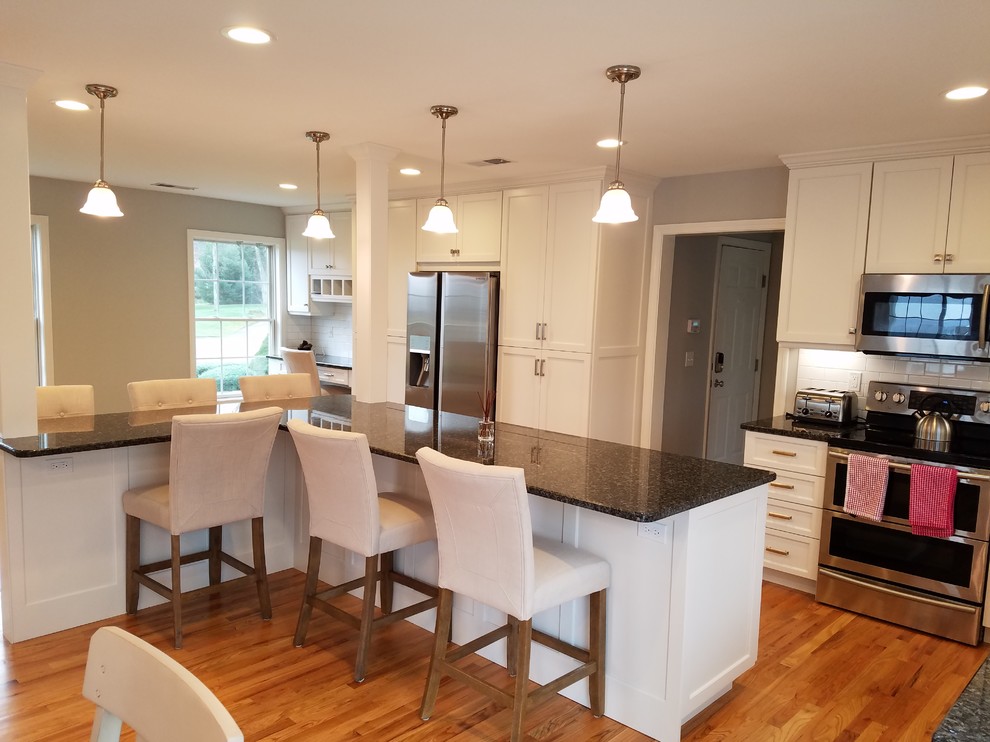 Example of a large transitional l-shaped light wood floor and brown floor eat-in kitchen design with an undermount sink, shaker cabinets, white cabinets, granite countertops, white backsplash, subway tile backsplash, stainless steel appliances and an island