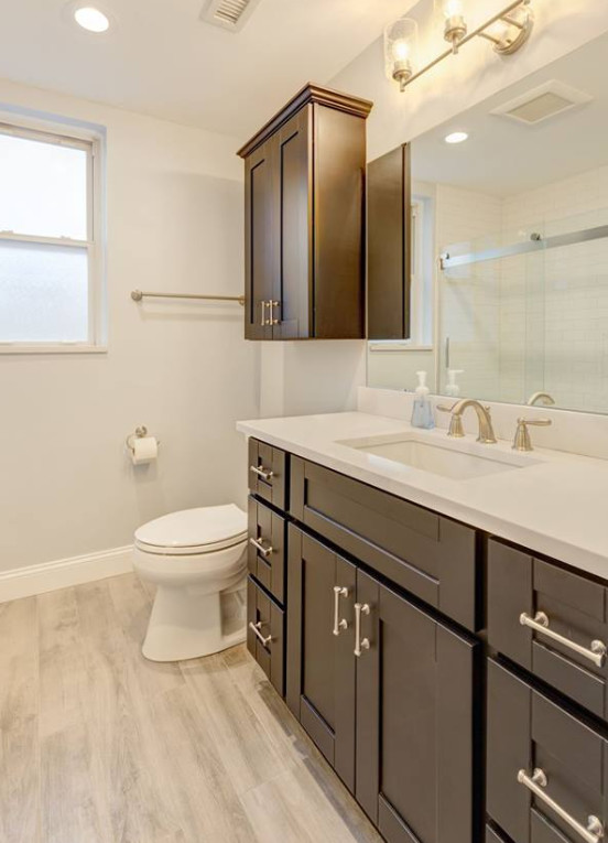 Photo of a small modern 3/4 bathroom in Other with shaker cabinets, brown cabinets, a corner tub, a shower/bathtub combo, a one-piece toilet, white tile, porcelain tile, beige walls, laminate floors, an undermount sink, quartzite benchtops, a sliding shower screen and white benchtops.